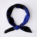 A black silk scarf with a vibrant blue paisley pattern, tied in a knot and displayed on a clean white background.
