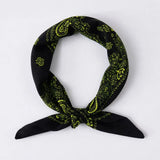 A black bandana scarf with a bright lime yellow paisley pattern, tied in a loop with the ends knotted, shown on a plain light gray background.