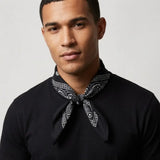 Man wearing a black shirt with a patterned bandana around his neck against a plain background