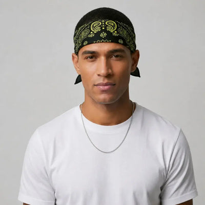 A man wearing a black bandana with a yellow paisley pattern and a white t-shirt, photographed against a light gray background.
