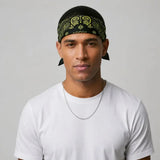 A man wearing a black bandana with a yellow paisley pattern and a white t-shirt, photographed against a light gray background.
