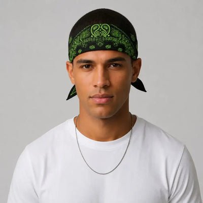 A man wearing a black and green paisley bandana headwrap and a white t-shirt, photographed against a neutral gray background.