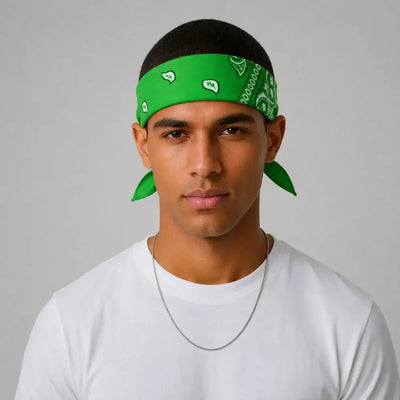 A man wearing a bright green bandana headwrap with a white paisley pattern, styled with a black cap and a white t-shirt against a neutral gray background.