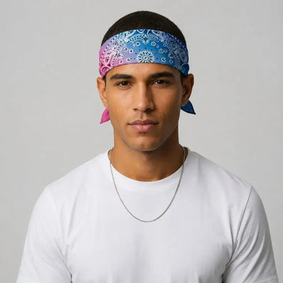 A man wearing a blue and pink paisley bandana headwrap with a white t-shirt and a silver chain necklace, photographed against a neutral light gray background.