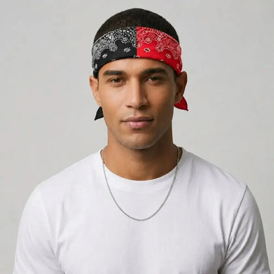 A man wearing a split-pattern headband with one side in black paisley and the other in red paisley, paired with a white t-shirt and a silver chain necklace, set against a plain light gray background.