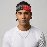 A man wearing a split-pattern headband with one side in black paisley and the other in red paisley, paired with a white t-shirt and a silver chain necklace, set against a plain light gray background.