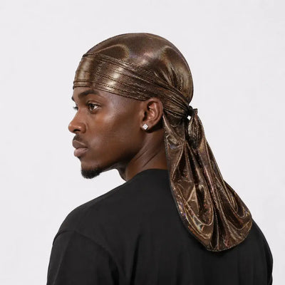A man shown in profile wearing a metallic bronze durag headwrap tied under his neck, paired with a black t-shirt against a light gray background.
