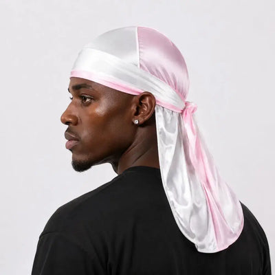 A man in profile wearing a shiny pink and white satin durag headwrap tied under the chin, paired with a black t-shirt against a light gray background.