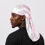A man in profile wearing a shiny pink and white satin durag headwrap tied under the chin, paired with a black t-shirt against a light gray background.