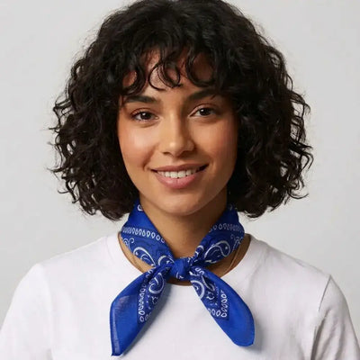 A woman with short curly dark hair wearing a white t-shirt and a blue paisley neck scarf, set against a plain light gray background.