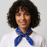 A woman with short curly dark hair wearing a white t-shirt and a blue paisley neck scarf, set against a plain light gray background.