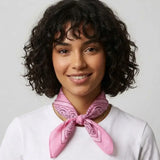 A woman with short curly dark hair wearing a white t-shirt and a pink paisley bandana tied around her neck, set against a plain light gray background.