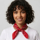 A woman with short curly dark hair wearing a red bandana tied around her neck and a white t-shirt, photographed against a light gray background.
